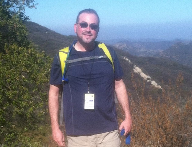 JSOM alum Glenn Egelman standing in front of a forest mountain and blue sky on a recent hiking trip