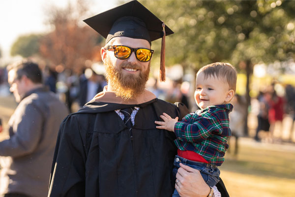 ut dallas jindal school graduate holding his child on commencement day