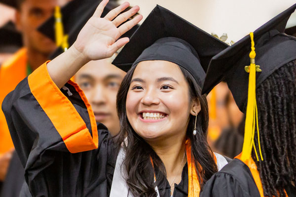 happy jindal school undergraduate waving in her cap and gown on ut dallas commencement